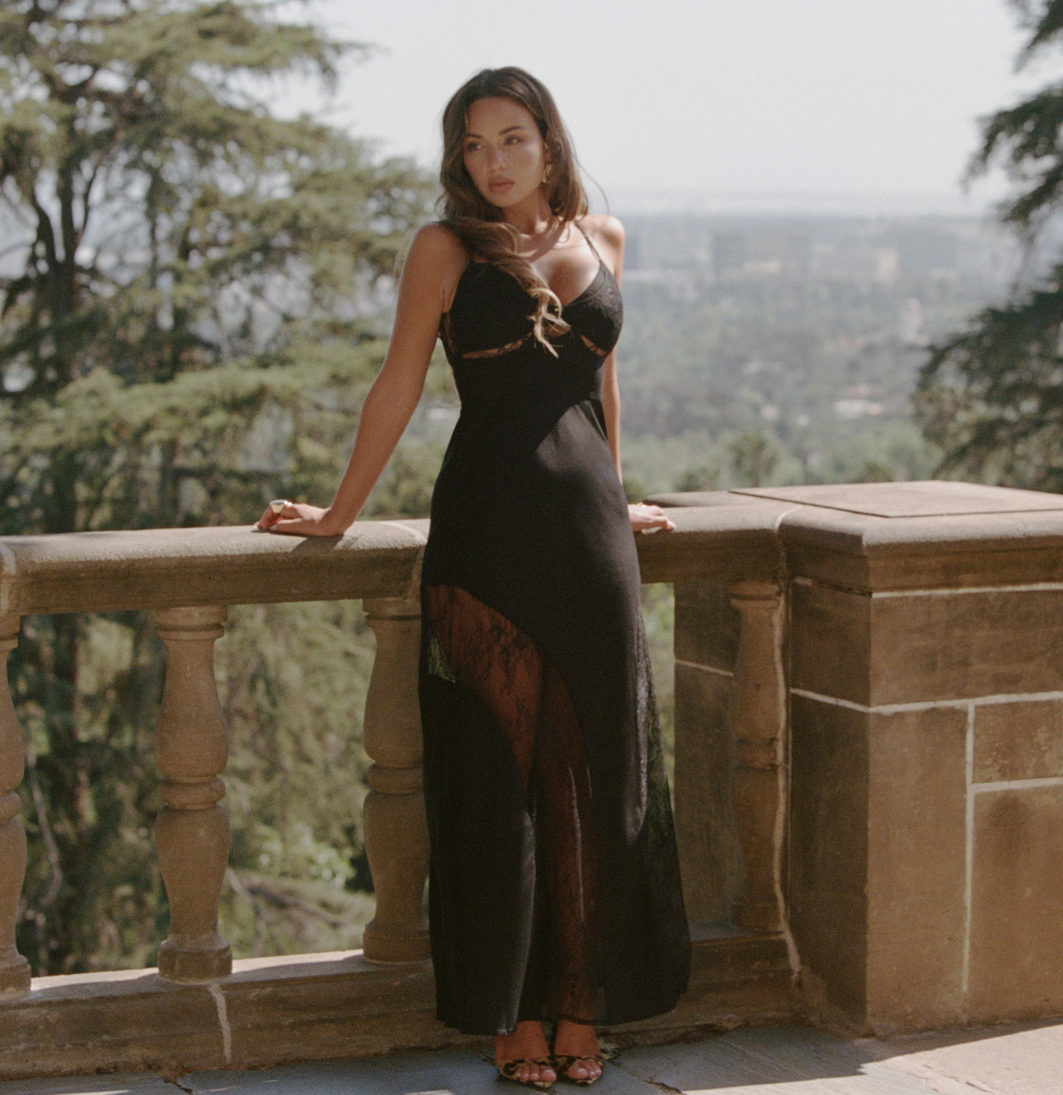 a woman in a black dress leaning on a stone railing