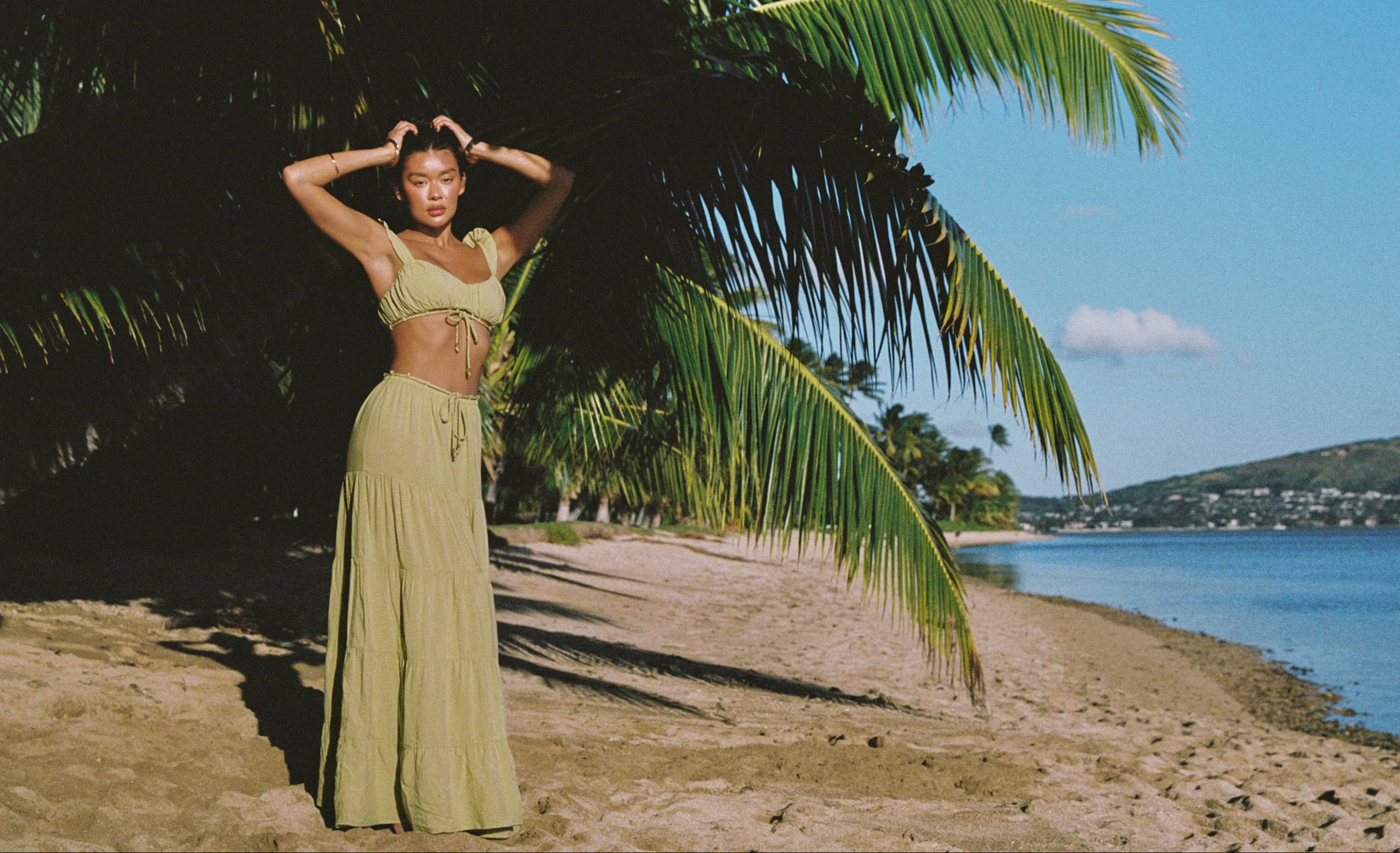 a woman in a green dress standing under a palm tree