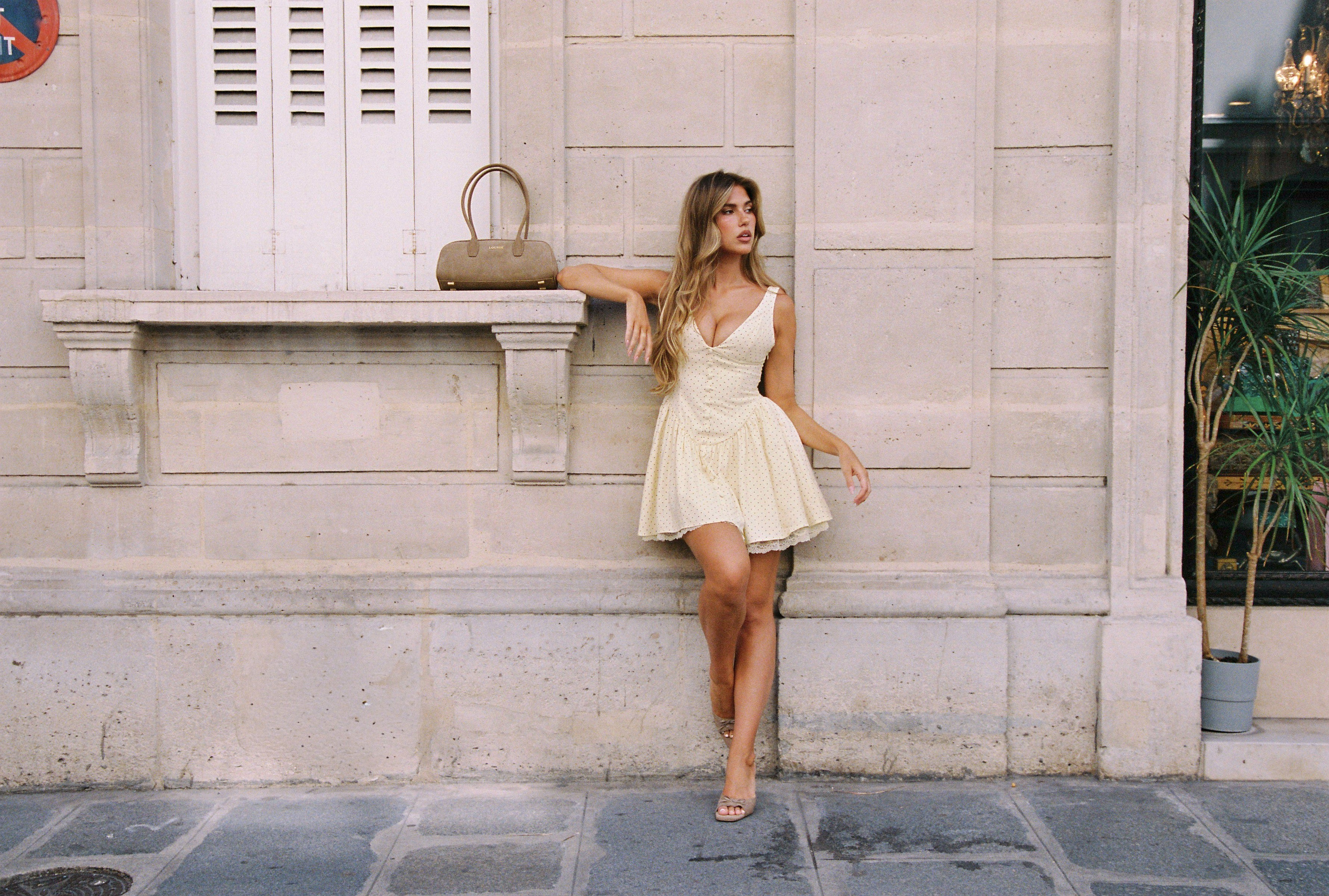a woman in a white dress leaning against a stone wall